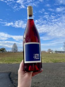 Hand holding a bottle of 2025 itä wines Carbonic Zinfandel with a bright blue sky and open fields in the background in Walla Walla, WA
